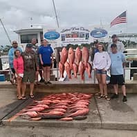 Large group displaying red snapper haul on dock at charter marina