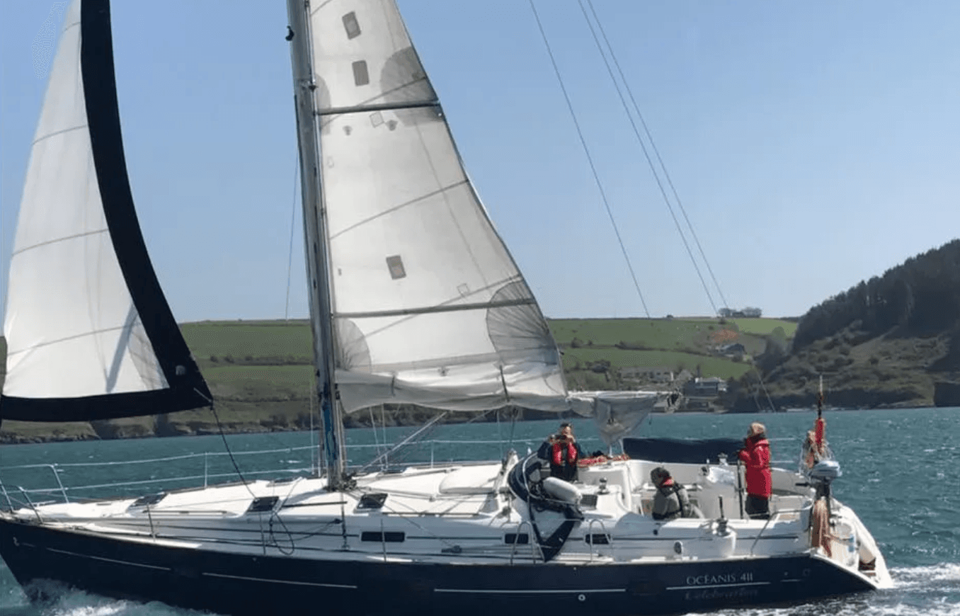 Coastal cruising yacht sailing near shoreline, day sailing experience