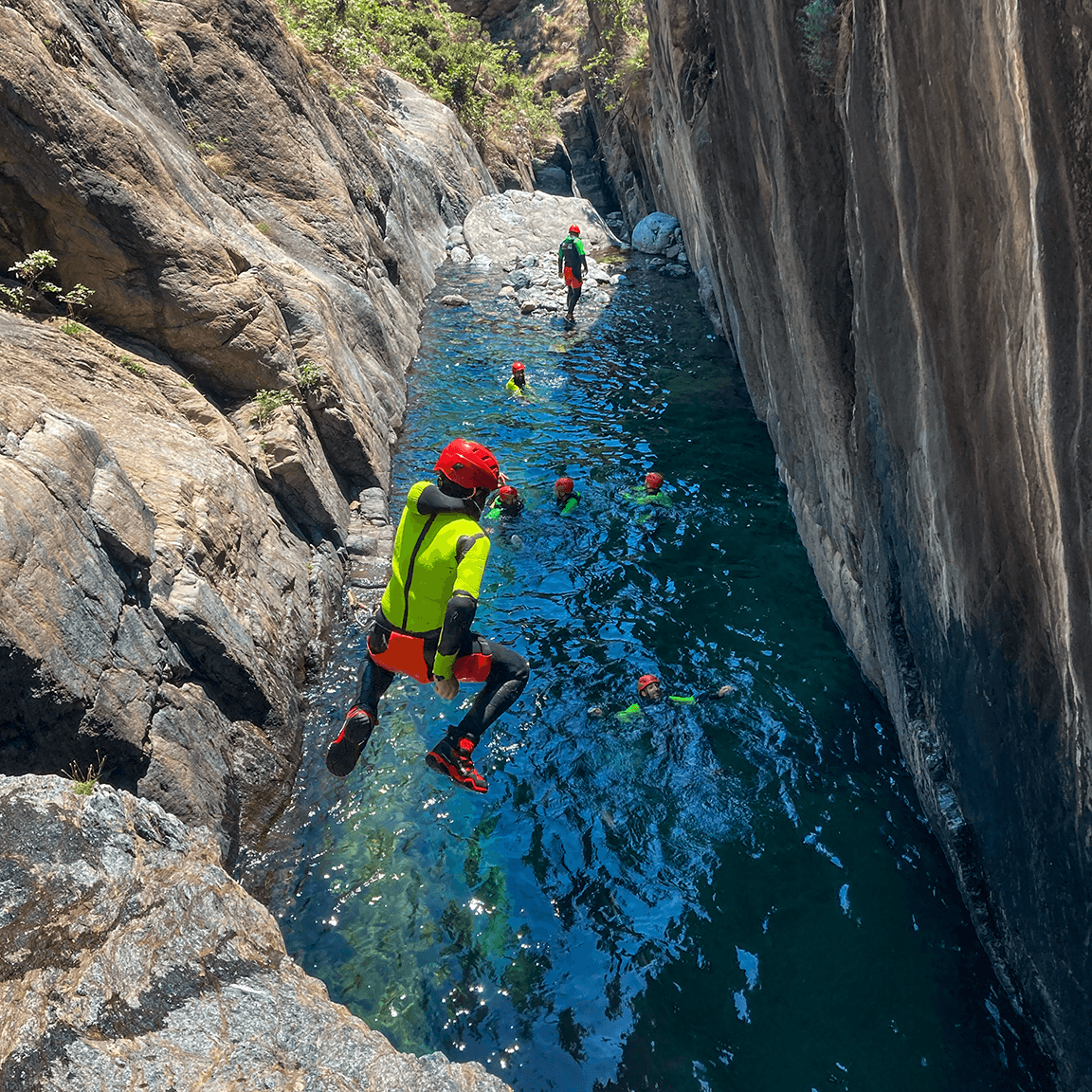 Group cliff jump into turquoise canyon pool during canyoning trip