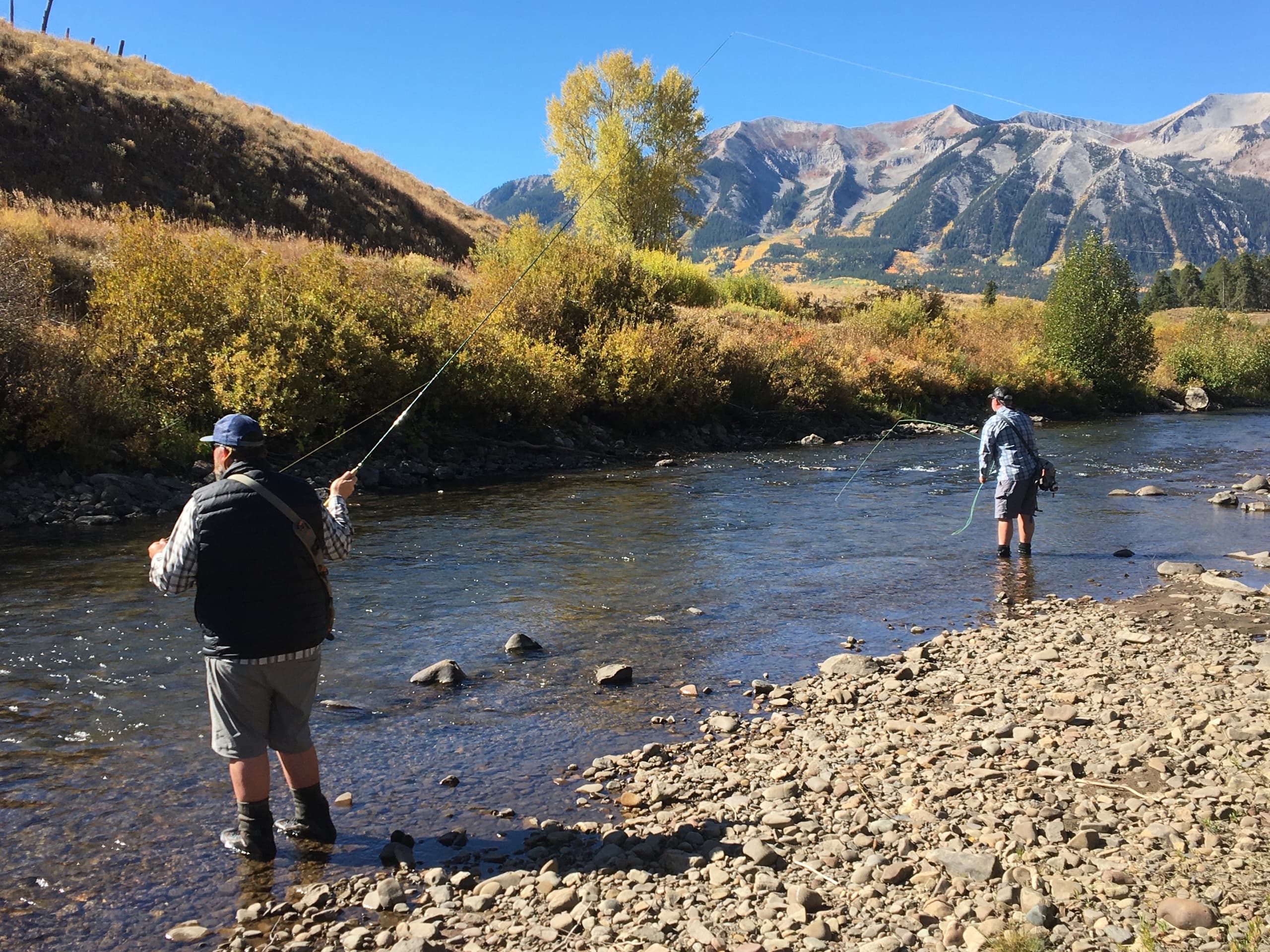 Anglers fly fishing in mountain river with alpine valley view
