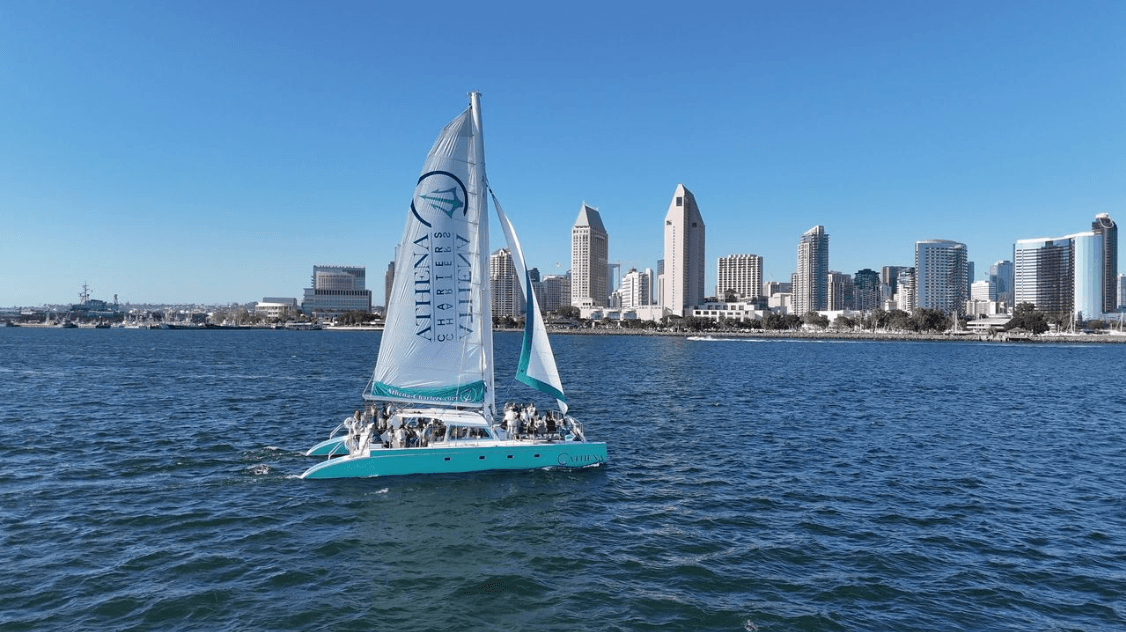 Turquoise catamaran sailing near San Diego waterfront skyline