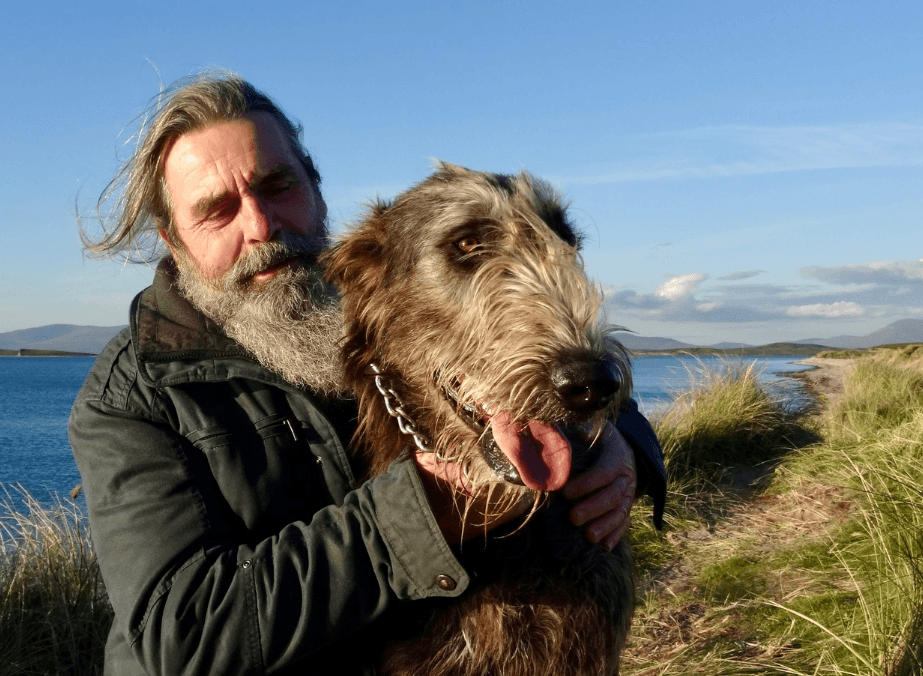 Man embracing large Irish wolfhound on coastal grassy headland