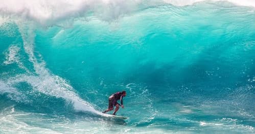 Surfer riding a turquoise barrel wave off Hawaiian coastline