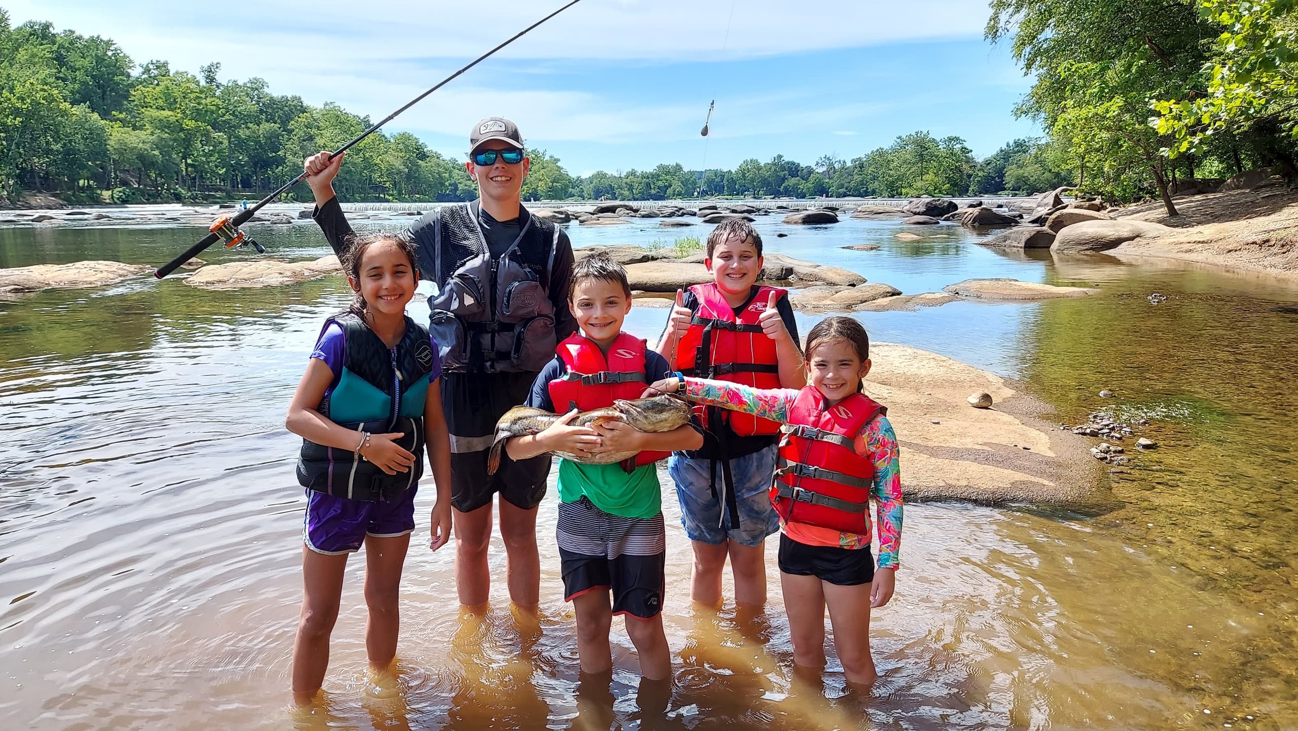 Family fishing with guide in shallow river near rocky riverbanks