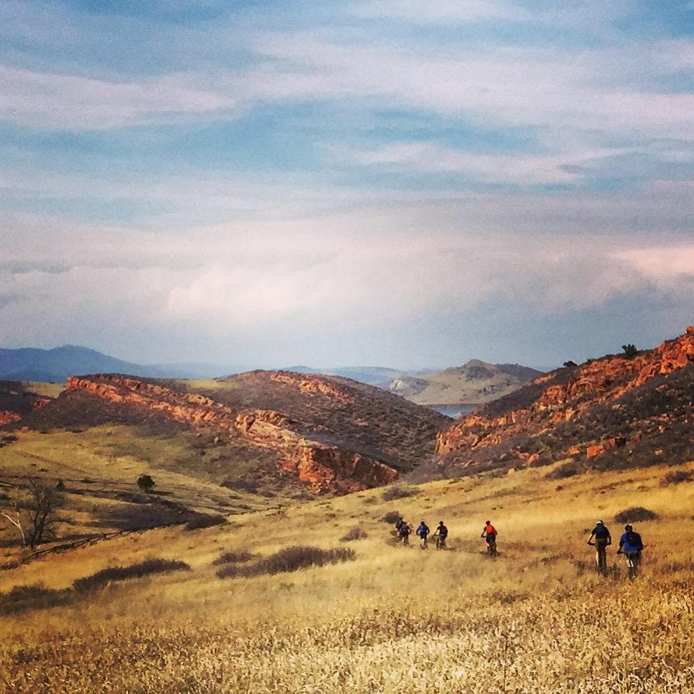 Mountain bikers traversing sunlit redrock ridgeline at sunset