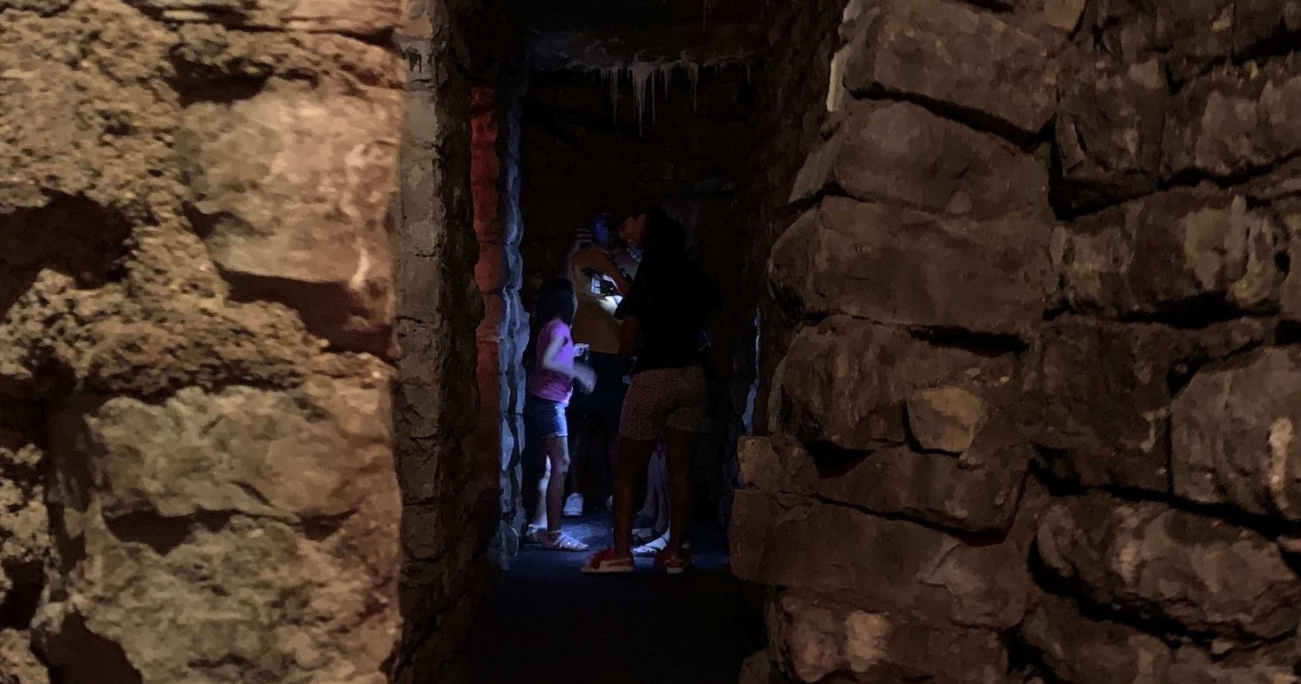 Visitors exploring narrow stone cave passage on guided tour