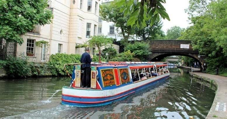 Narrowboat cruising under a brick bridge on a tree-lined canal