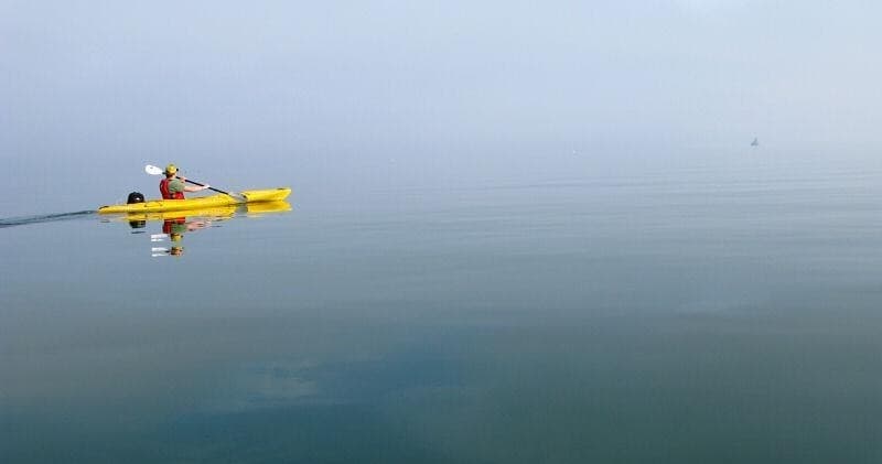 Solo yellow kayak reflected in glassy calm sea at sunrise