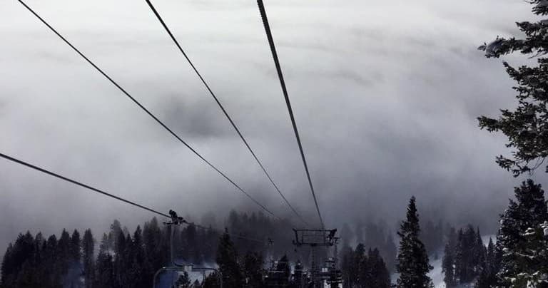 Ski lift cables stretching over foggy alpine forest and peaks