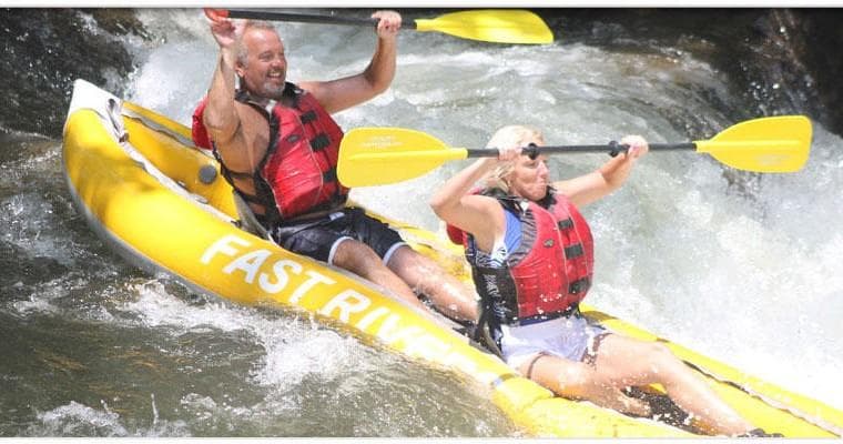 Couple riding yellow inflatable raft down Nantahala class III whitewater rapids