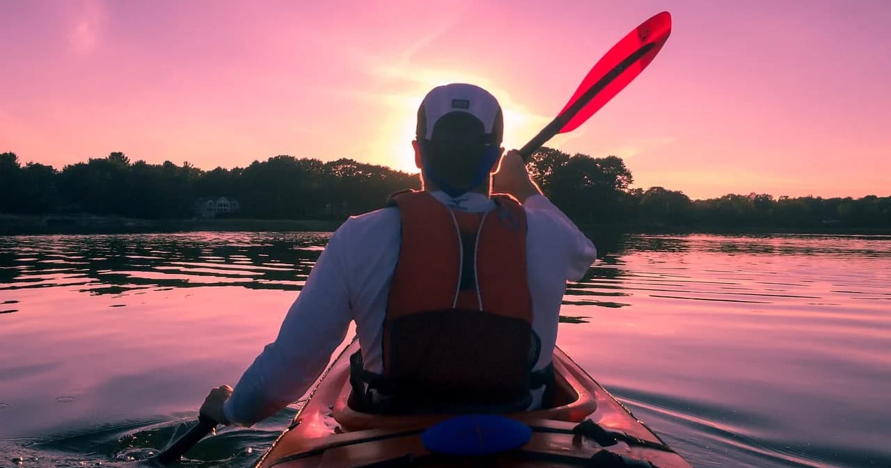 Kayaker paddling at sunset on calm lake with silhouetted shore