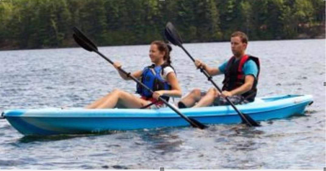 Two people kayaking tandem on calm tree-lined lake waters