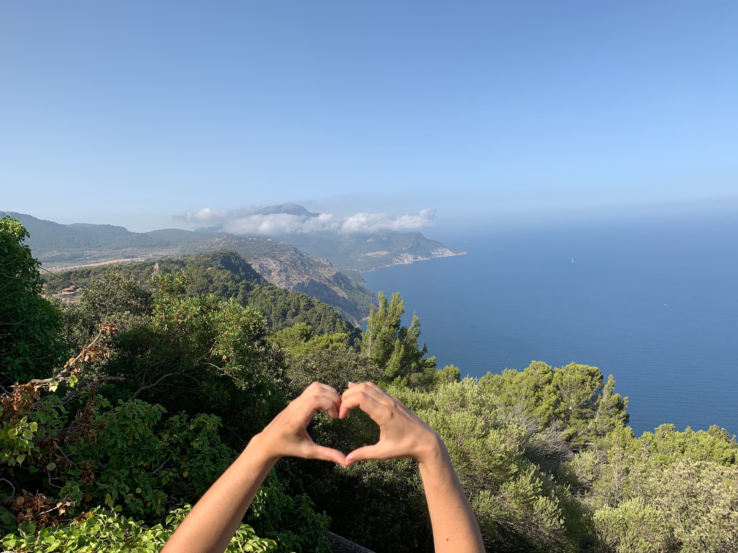 Hiker at Mediterranean coastal viewpoint making heart with hands