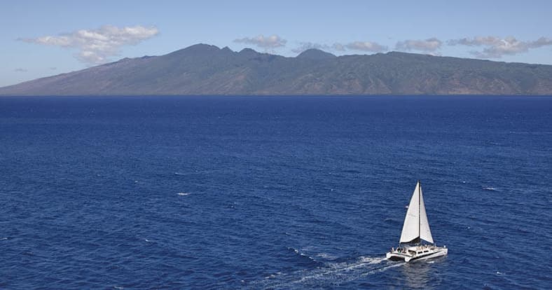 Sailboat sailing across deep blue ocean with island backdrop