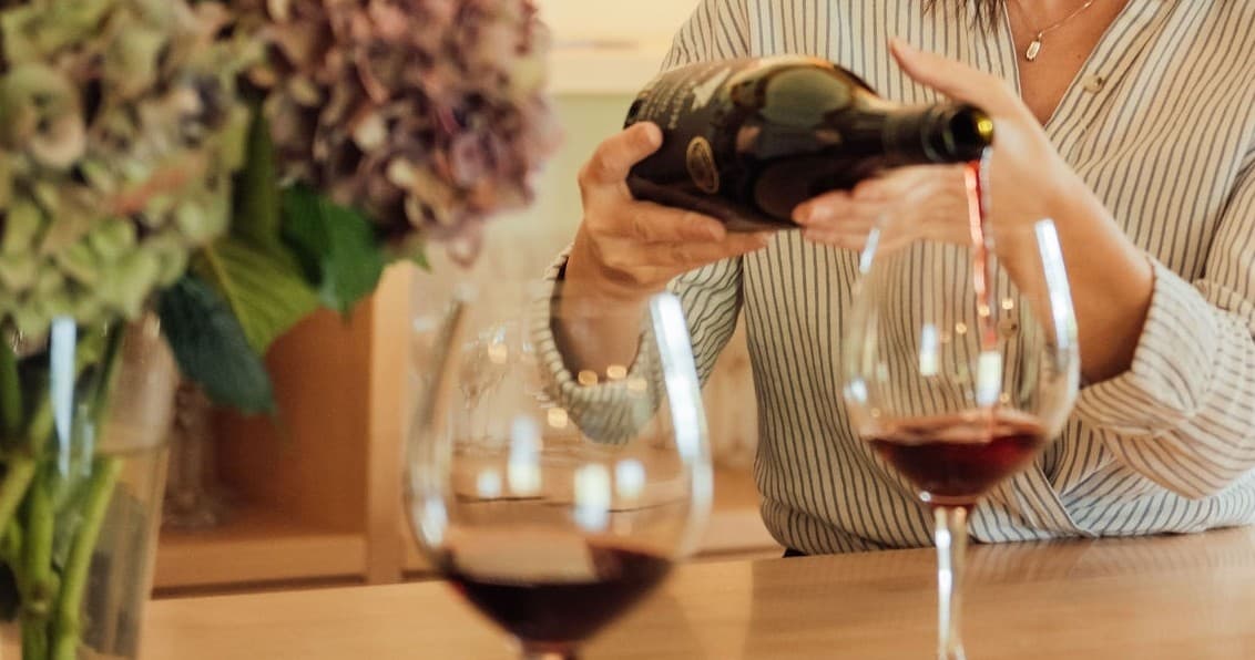 Close-up pouring red wine into glass at rustic tasting table, winery