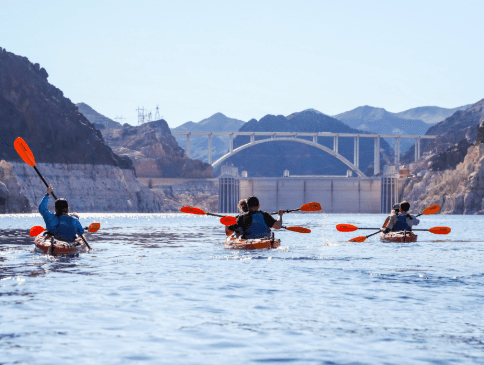 Kayakers paddling across canyon river with bridge backdrop