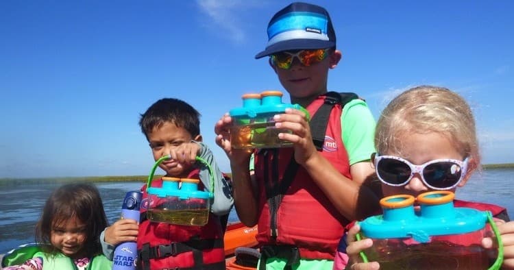 Children wearing lifejackets kayaking with binoculars on sunny day