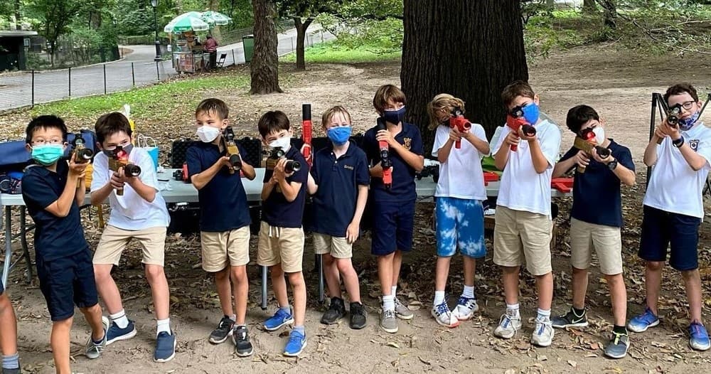 Kids playing outdoor nerf battle in park under trees