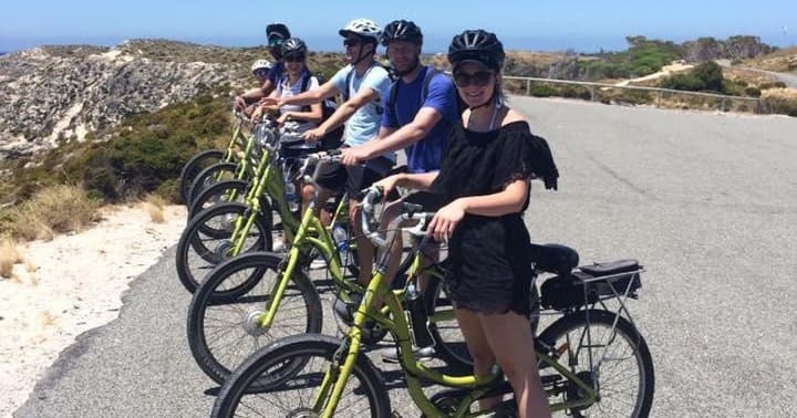 Group cyclists on coastal road tour, cliffside scenic biking