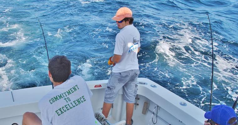 Two anglers fishing off stern with choppy blue ocean backdrop