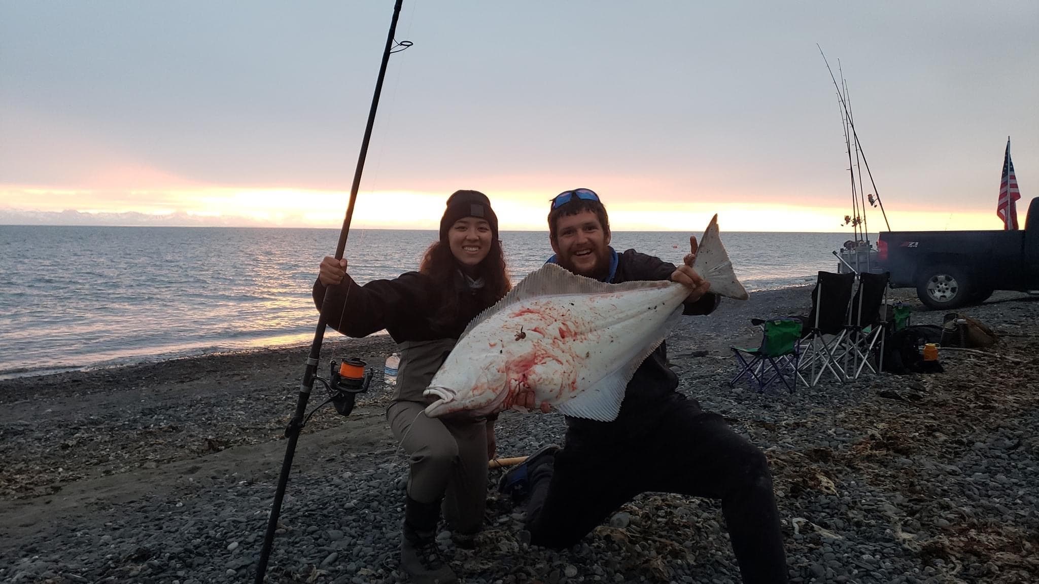 Two anglers celebrating beach catch at sunset on pebble shore
