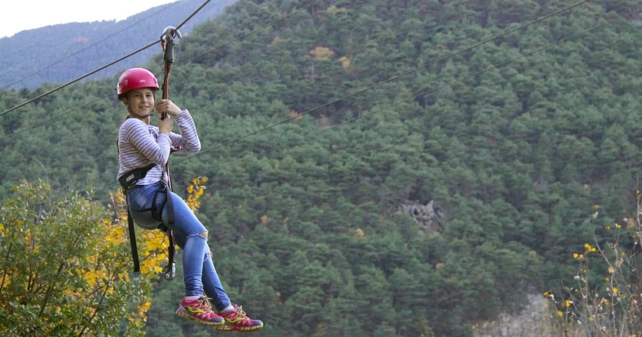 Woman ziplining across forested valley, suspended over trees