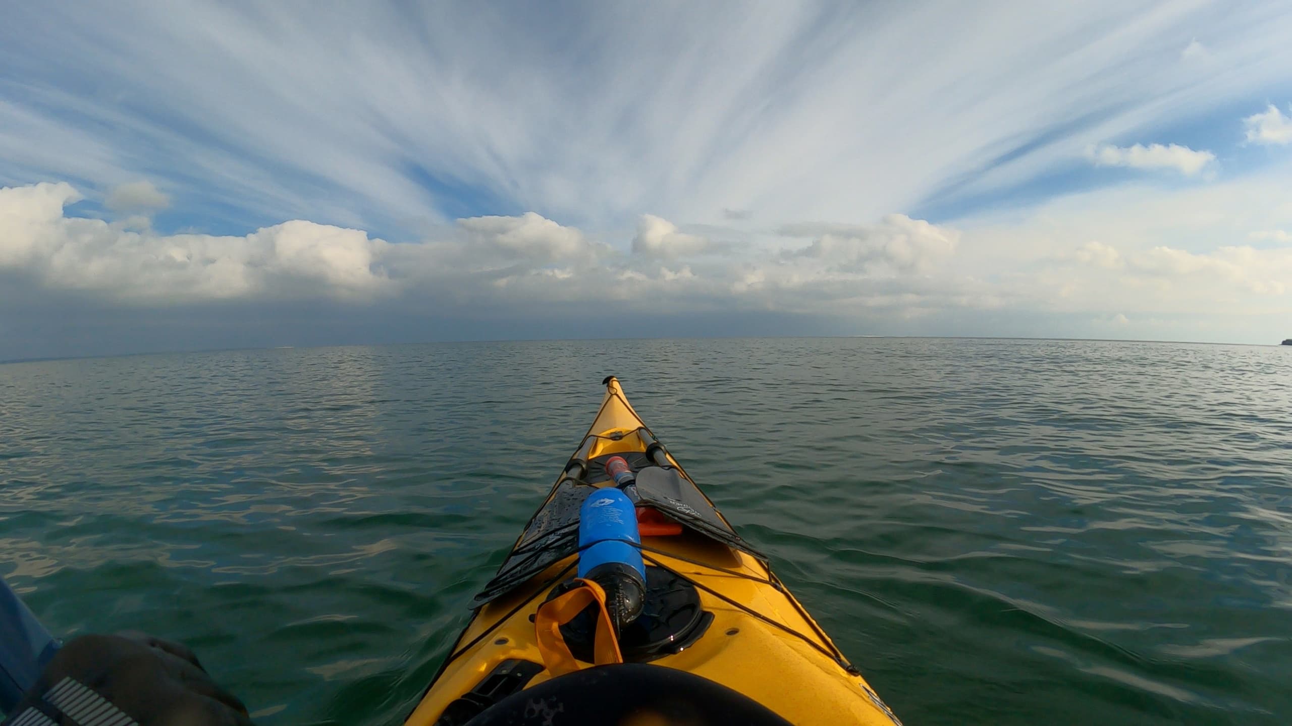 Sea kayak bow under dramatic cloudscape on open water excursion