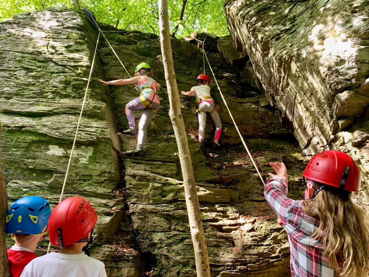 Young climbers scaling shaded sandstone cliff with helmets and ropes