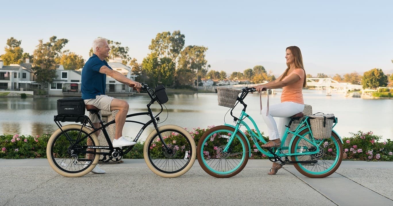 Couple riding electric bikes along lakeside promenade at sunset