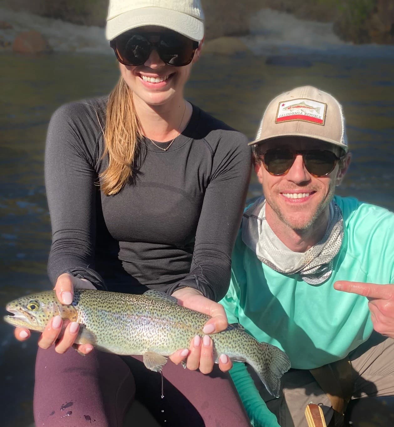 Couple holding trout on riverside during guided fly fishing trip