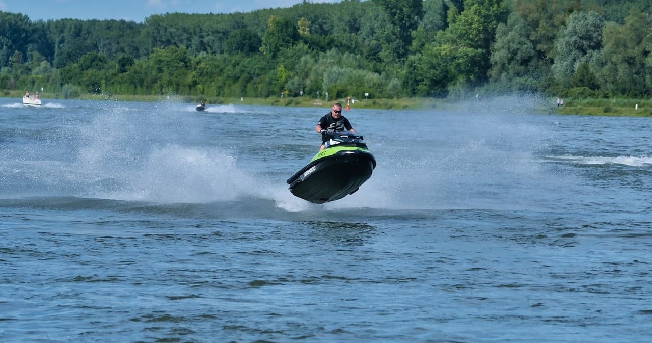 Jet ski rider jumping over river waves near forested shoreline