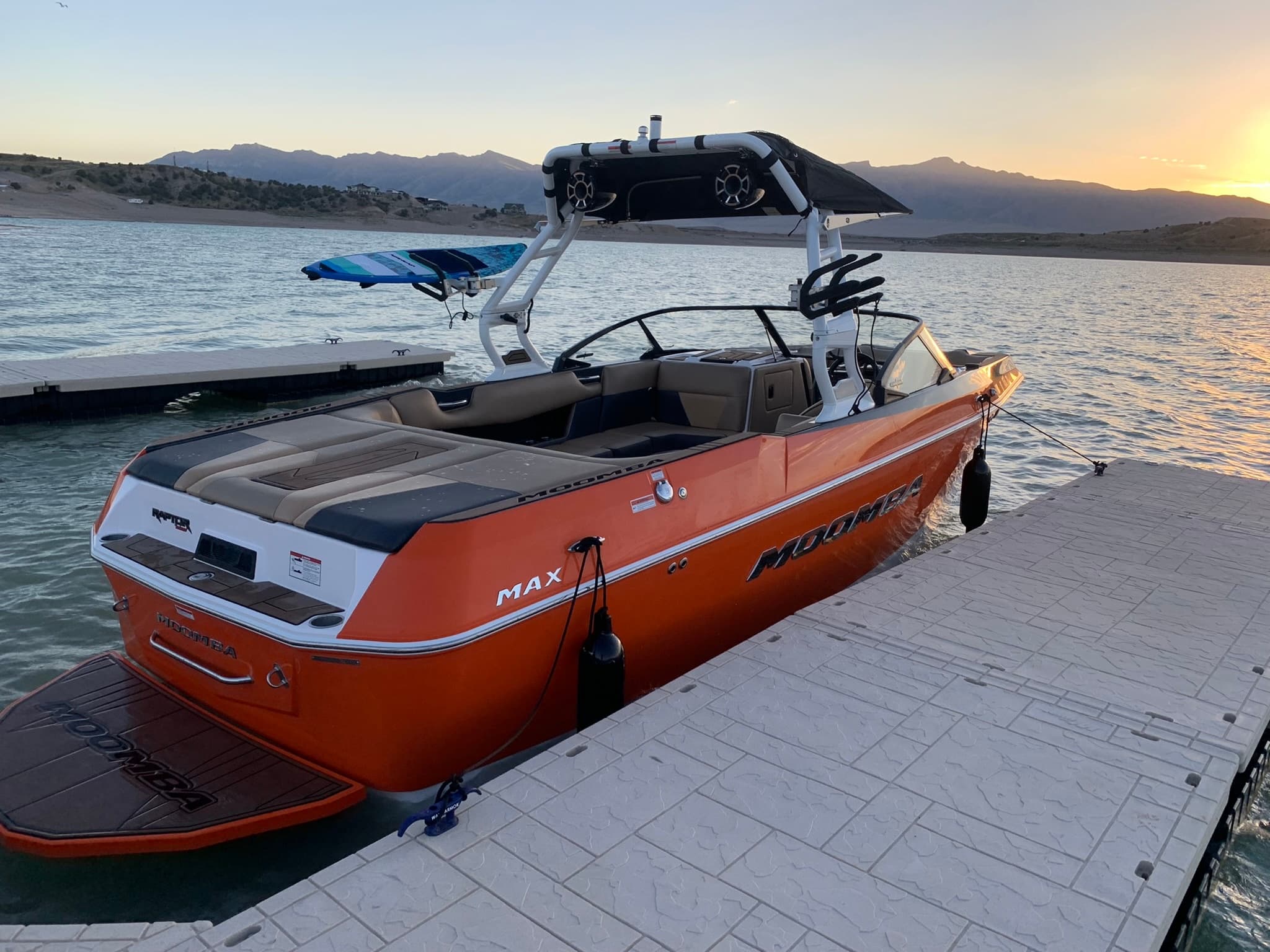 Orange wakeboat docked at sunset on mountain lake for watersports