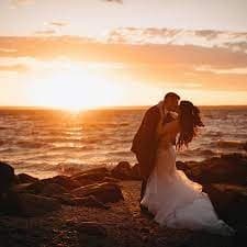 Couple embracing on rocky shoreline at sunset, romantic scene