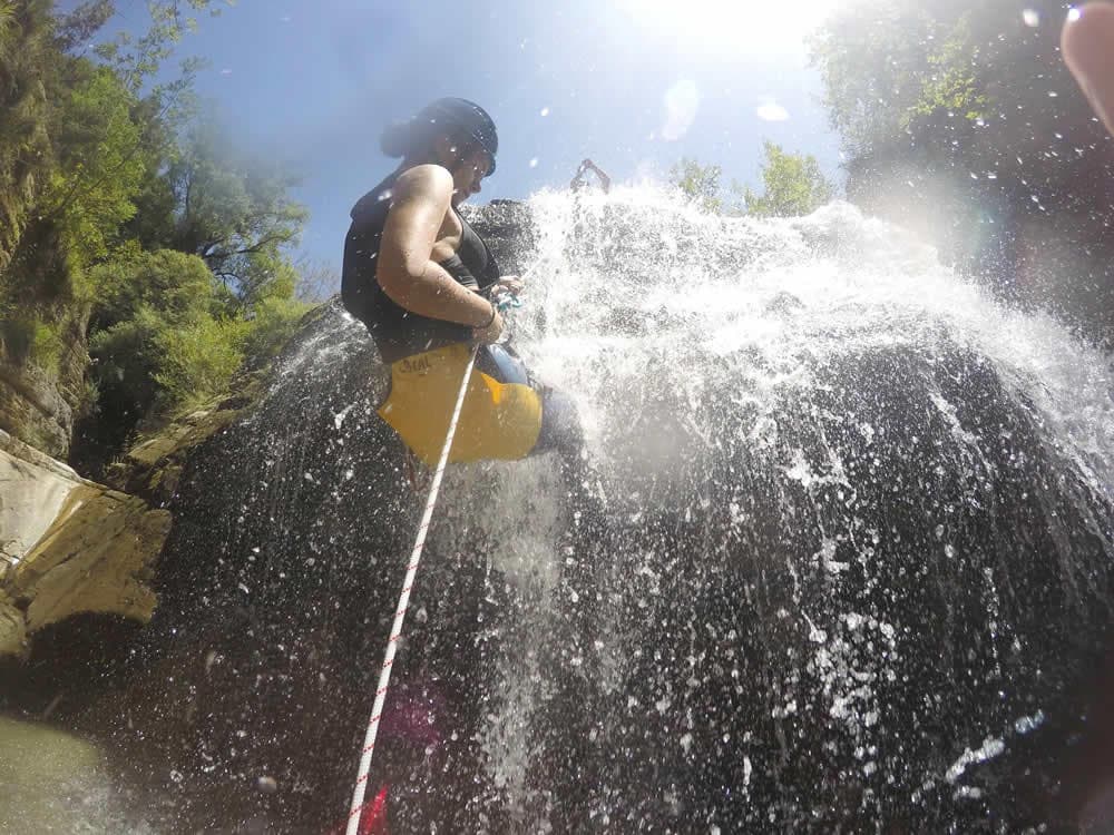 Canyoning action: person rappelling down waterfall in canyon