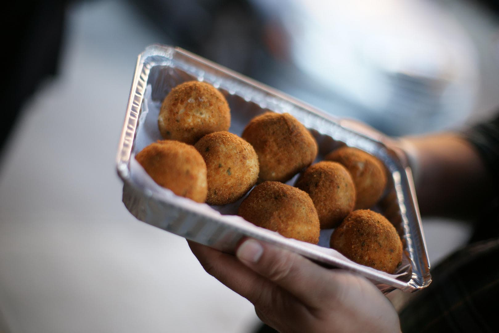 Hands holding tray of fried croquettes at NYC street food stall