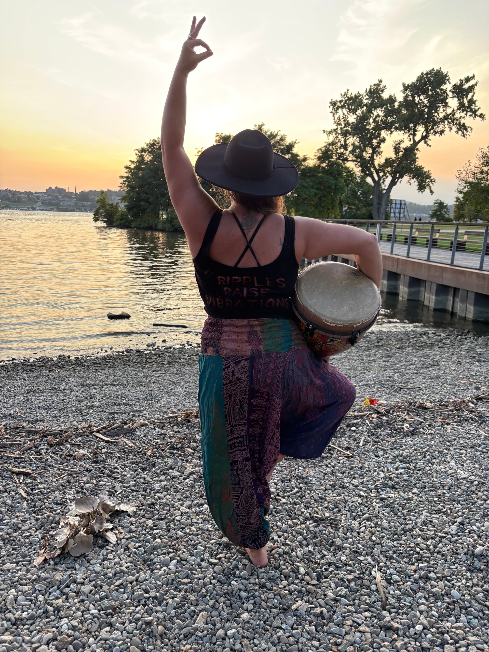 Woman playing frame drum at sunset on rocky river shore