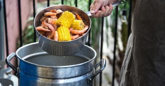 Outdoor shrimp boil: corn and shrimp drained into pot