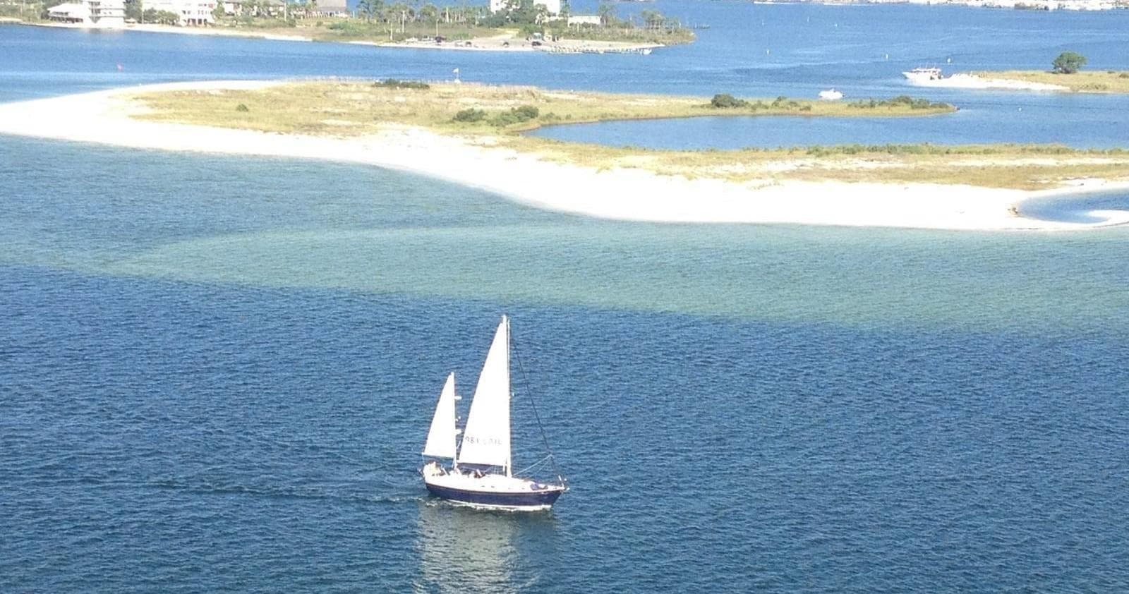 Small sailboat sailing near coastal sandbars in clear blue water