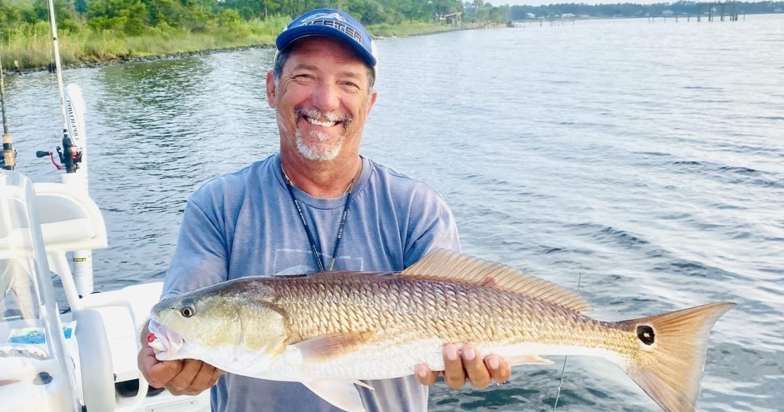 Angler smiling on boat holding large redfish in coastal waters