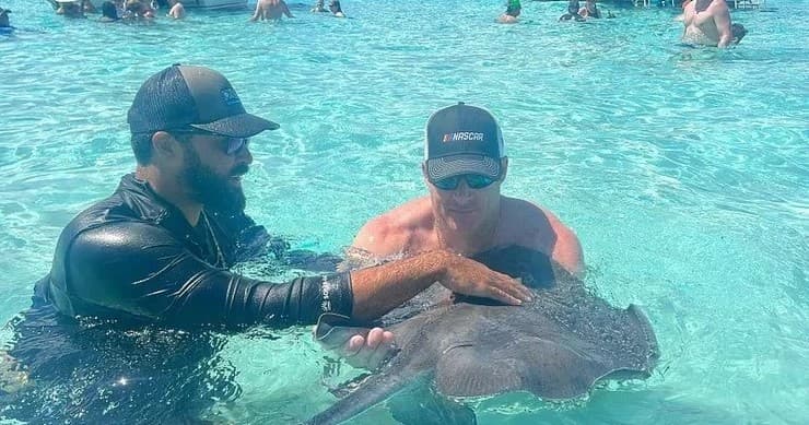 Tourists handling stingray in clear shallow tropical water