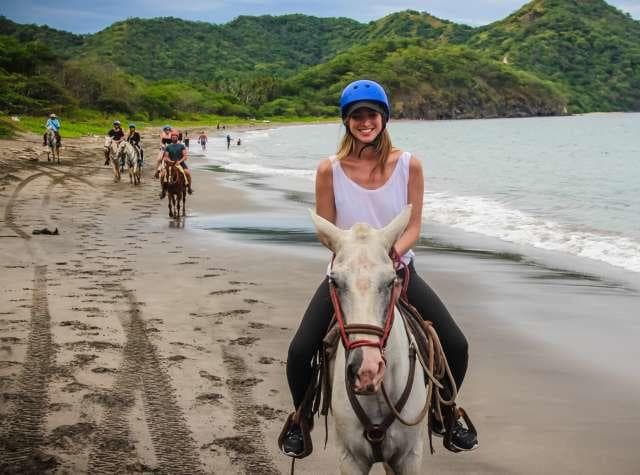 Rider horseback on sandy beach with tropical hills and ocean