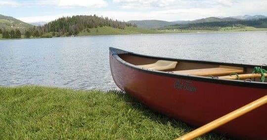 Red canoe pulled ashore on grassy lakeside, mountain backdrop