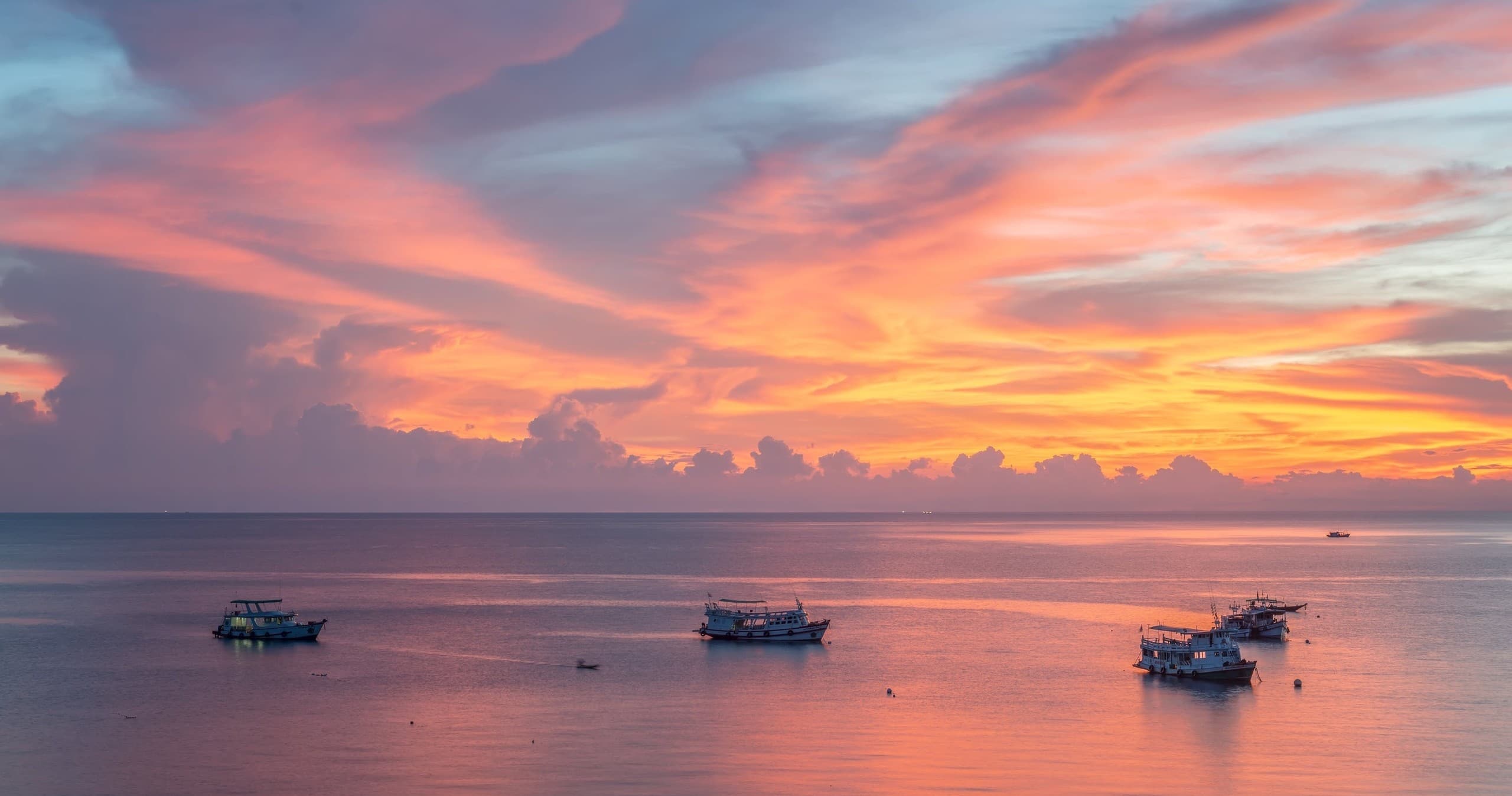 Sunset over calm ocean with anchored boats, tropical seascape