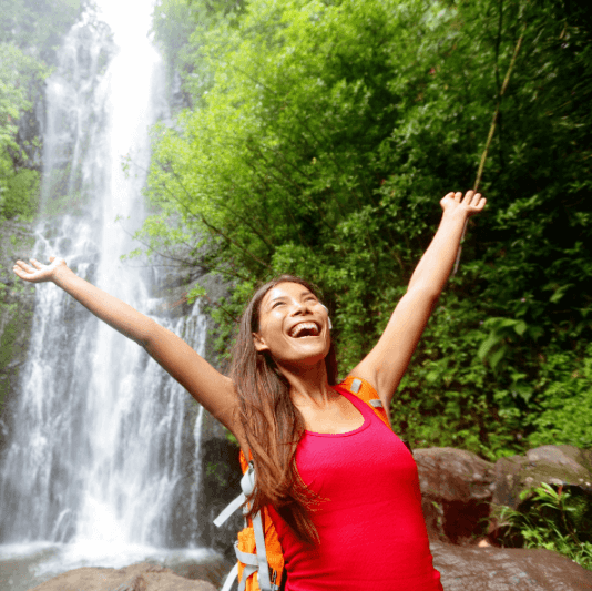 Smiling hiker celebrating near a waterfall in tropical rainforest