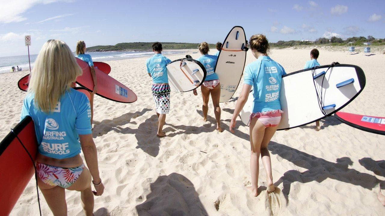 Surfers carrying boards across sunny sandy beach toward ocean