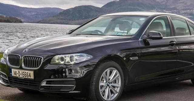 Black BMW parked by lakeshore with scenic hills for guided tours