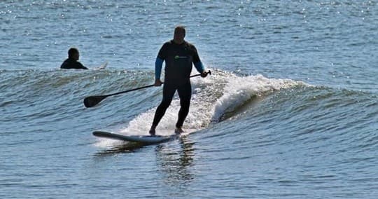 Stand-up paddler surfing a small ocean wave near shoreline