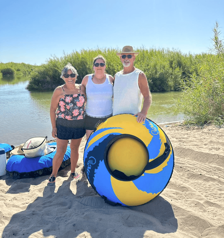 Three rafters posing with colorful inflatable tube by riverbank