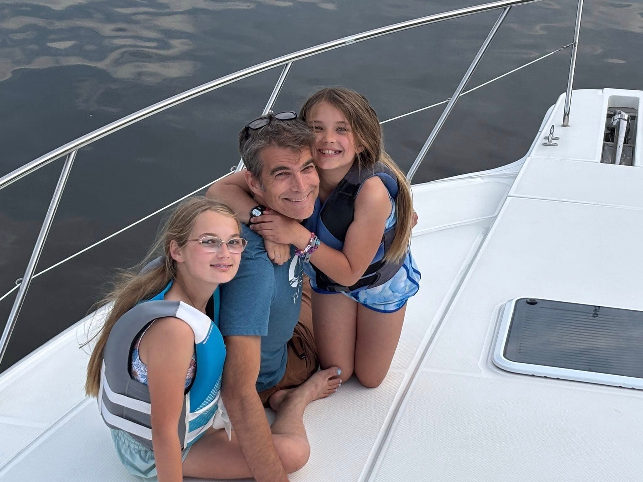 Family on yacht bow wearing life jackets enjoying coastal cruise