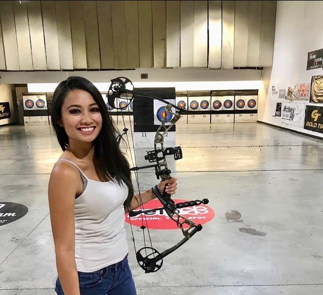 Woman holding compound bow smiling inside indoor archery range